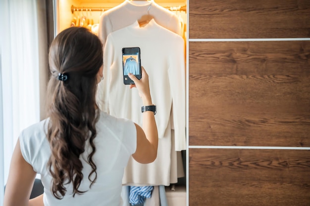 Foto mujer joven tomando fotos de ropa vieja no deseada para la venta en una aplicación de teléfono inteligente