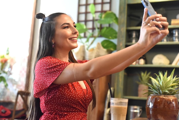 Mujer joven tomando selfie en una cafetería.