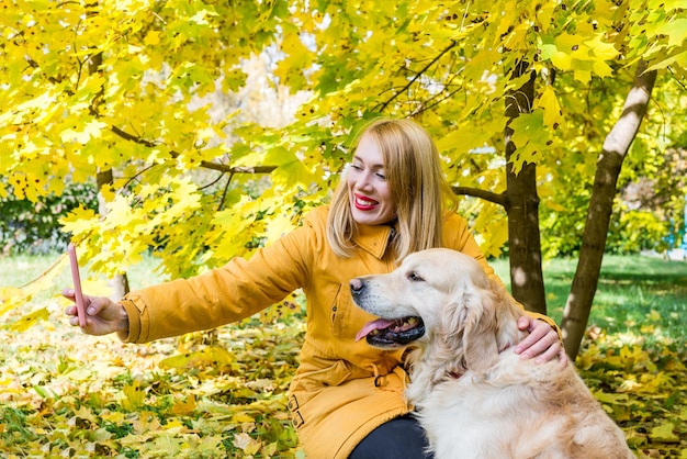 Mujer joven tomando selfie junto con su perro en el parque. Cuidado de mascotas
