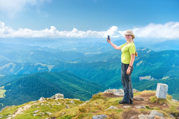 Mujer joven tomando selfie en smartphone en el acantilado de las montañas