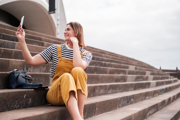 Mujer joven tomando un selfie con su teléfono inteligente en unas escaleras al aire libre Concepto de estilo de vida al aire libre teléfono inteligente