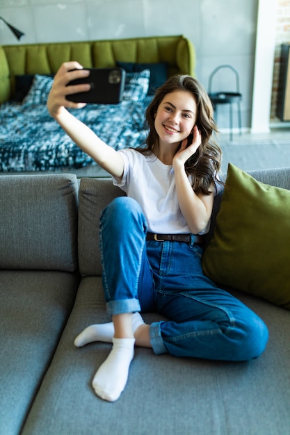 Mujer joven tomando selfie con su teléfono mientras está sentado en la sala de estar.