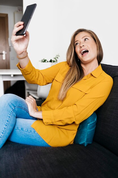 Foto mujer joven tomando selfies con teléfono móvil mientras está sentada en el sofá en casa