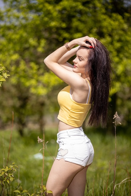 Mujer joven en top amarillo y pantalones cortos blancos de pie en la naturaleza en verano