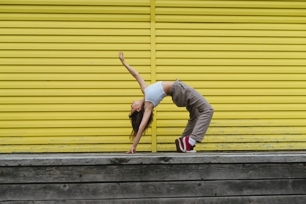 Foto mujer joven en top blanco y pantalones de lino bailando frente a la pared amarilla