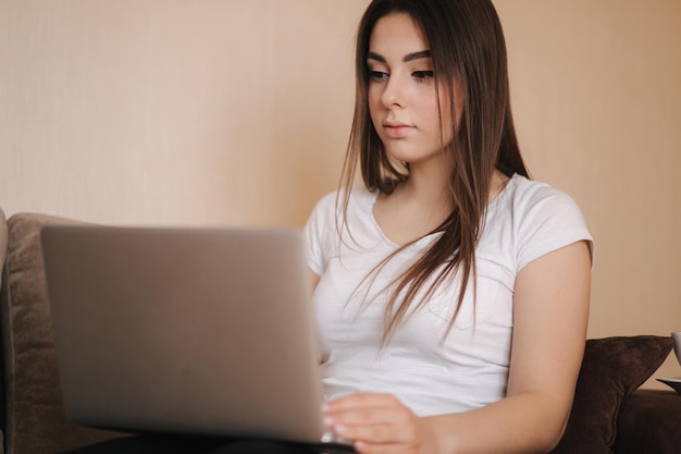 Mujer joven trabaja en casa en cuarentena Mujer usa computadora portátil en el sofá Mujer estudia aprendizaje a distancia