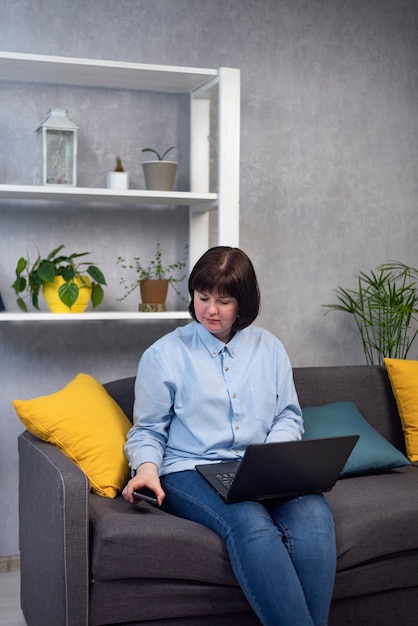 Mujer joven trabaja en una computadora portátil mientras está sentado en el sofá en casa. Freelancer en la oficina en casa. Trabajar en baja por maternidad