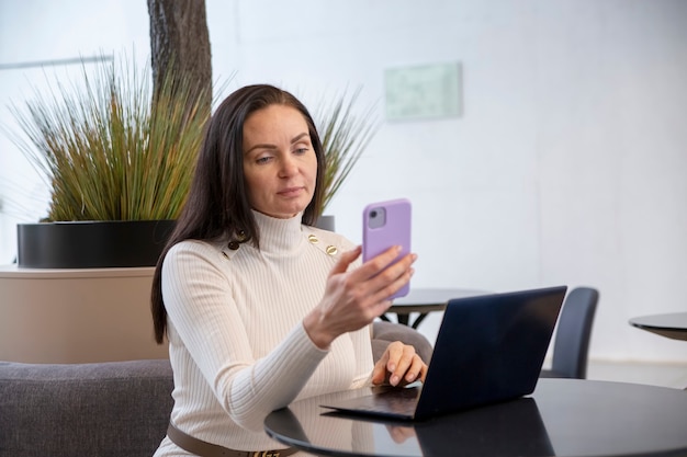 Mujer joven trabaja en una computadora portátil y un teléfono inteligente en la cafetería.