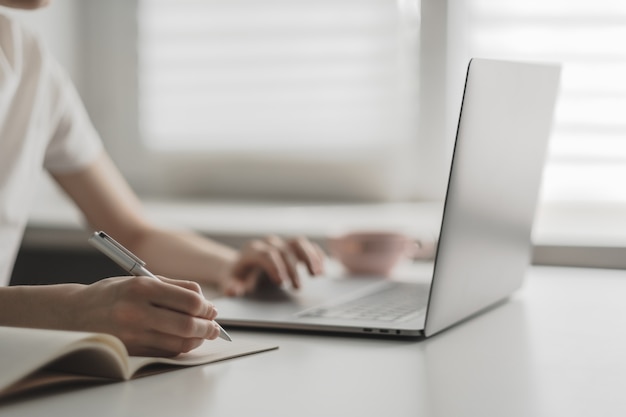 Mujer joven trabaja en una computadora portátil y toma notas en un cuaderno