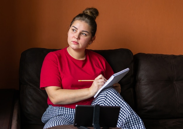 Mujer joven trabaja y estudia en línea a través de una videoconferencia en una tableta. Educación a distancia y trabajo desde casa.