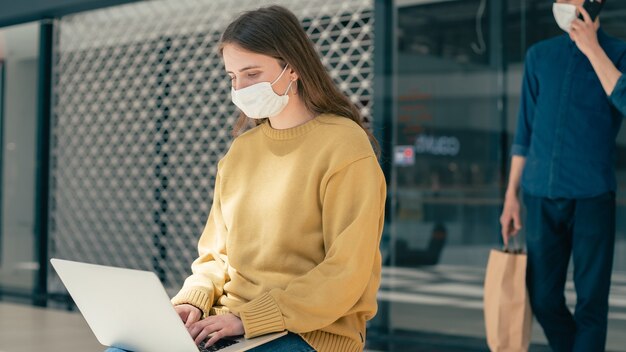 Foto mujer joven está trabajando en una computadora portátil mientras está sentada fuera de un edificio de la ciudad. pandemia en la ciudad