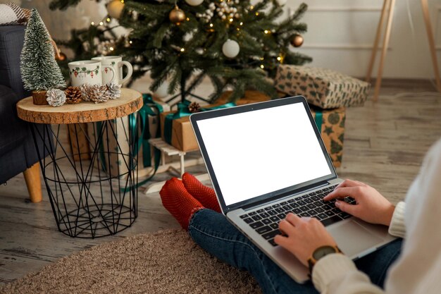 Mujer joven trabajando en una computadora portátil con pantalla en blanco con espacio de copia de maqueta Diseño interior de la sala de estar de la casa moderna Espacio de trabajo decorado para Navidad y Año Nuevo