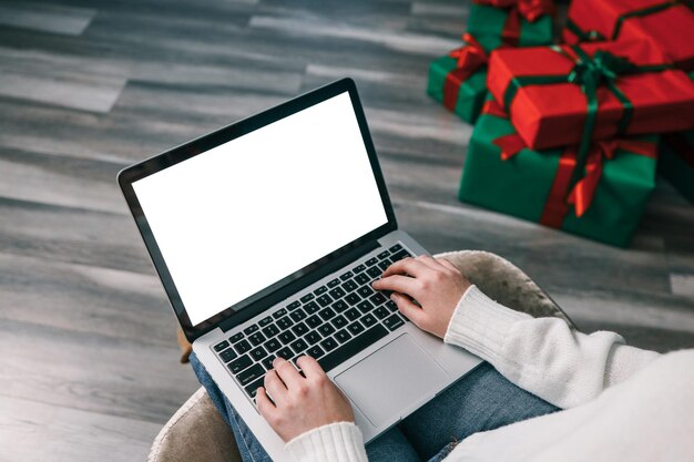 Mujer joven trabajando en una computadora portátil con pantalla en blanco con espacio de copia de maqueta Diseño interior de la sala de estar de la casa moderna Espacio de trabajo decorado para Navidad y Año Nuevo