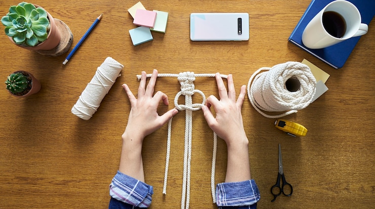 Foto mujer joven trabajando una decoración de macramé artesanal sobre un escritorio de madera