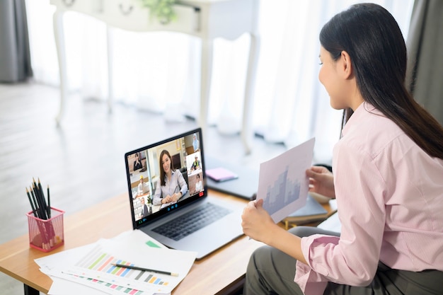 Mujer joven está trabajando con la pantalla de su computadora durante una reunión de negocios a través de la aplicación de videoconferencia.