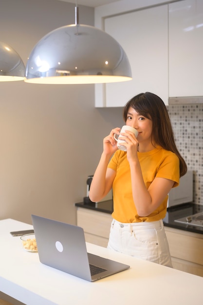 Una mujer joven trabajando con su computadora portátil y tomando una taza de café, estilo de vida y concepto de negocio