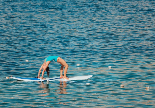 Mujer joven en traje de baño azul haciendo yoga en una tabla con remo