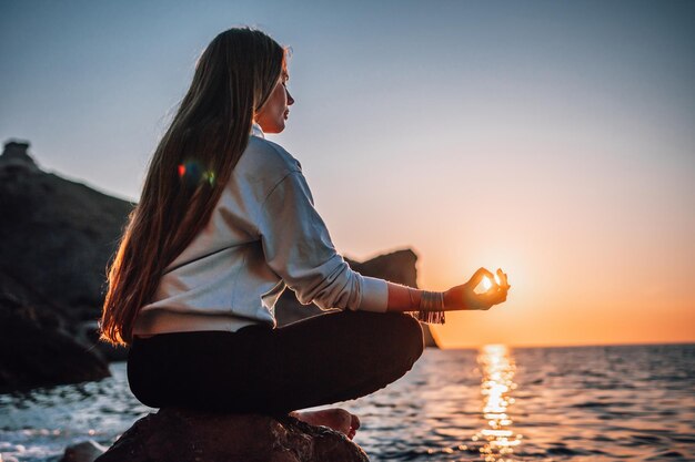 Mujer joven en traje de baño con cabello largo practicando estiramientos al aire libre en una estera de yoga junto al mar en un día soleado Rutina de pilates de fitness de yoga para mujeres Concepto de armonía y meditación de estilo de vida saludable