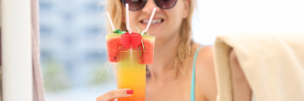 Mujer joven en traje de baño y gafas de sol bebiendo cócteles en primer plano de vacaciones