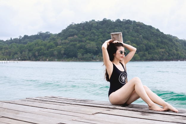 Mujer joven en el traje de baño que toma el sol en la playa del embarcadero en el mar, concepto de las vacaciones de verano.