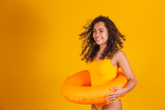 Mujer joven en traje de baño sosteniendo un flotador naranja con cara feliz de pie y sonriendo con una sonrisa segura mostrando los dientes. Concepto de vacaciones y diversión