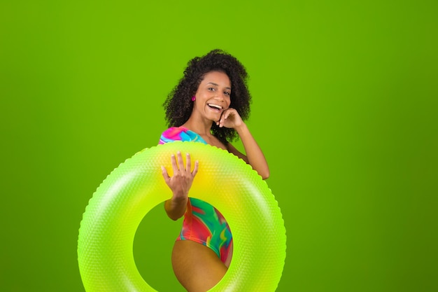 Mujer joven en traje de baño sosteniendo un flotador verde con cara feliz de pie y sonriendo con una sonrisa segura mostrando los dientes Espacio de copia de concepto de vacaciones y diversión