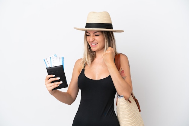 Mujer joven en traje de baño sosteniendo un pasaporte aislado sobre fondo blanco celebrando una victoria