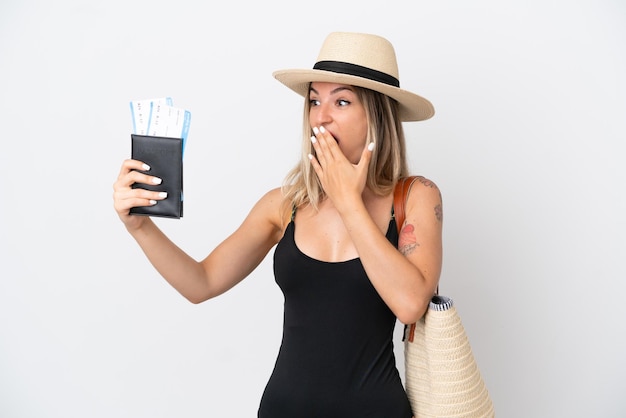 Mujer joven en traje de baño sosteniendo un pasaporte aislado sobre fondo blanco con sorpresa y expresión facial conmocionada