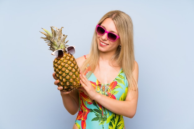 Mujer joven en traje de baño sosteniendo una piña con gafas de sol