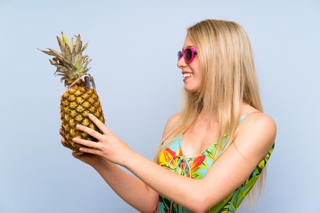 Mujer joven en traje de baño sosteniendo una piña con gafas de sol