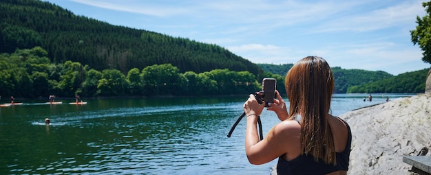 Una mujer joven en traje de baño tomando fotos de un lago y un bosque