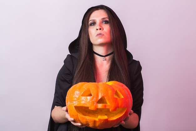 Mujer joven en traje de bruja de Halloween en estudio con calabaza amarilla.
