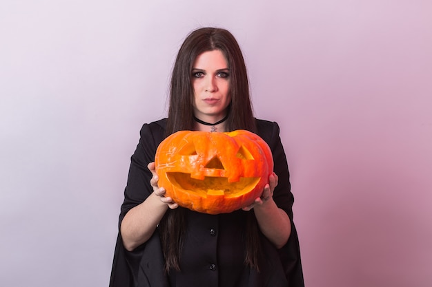 Mujer joven en traje de bruja de Halloween en estudio con calabaza amarilla.