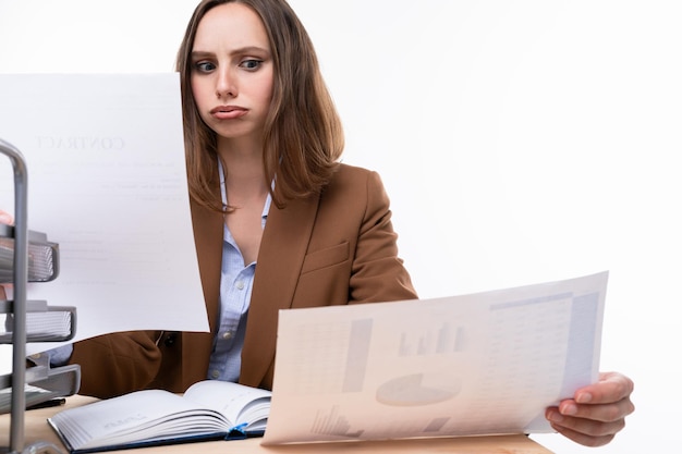 Una mujer joven con un traje elegante está estudiando documentos mientras está sentada en su lugar de trabajo Resolviendo problemas de negocios en la oficina Disparos de estudio sobre un fondo blanco