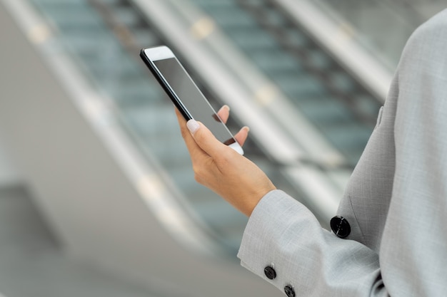 Mujer joven en traje gris con smartphone contra escaleras mecánicas