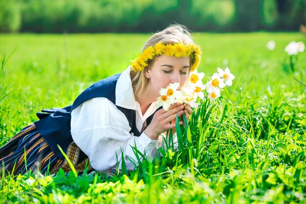 Mujer joven en traje nacional en un campo con flores de narcisos