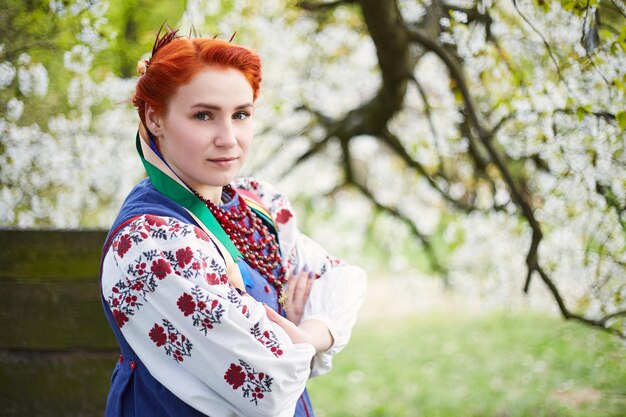 Mujer joven en traje nacional ucraniano Sonriente joven dama en ropa tradicional Manténgase cerca del árbol floreciente Paz en Ucrania