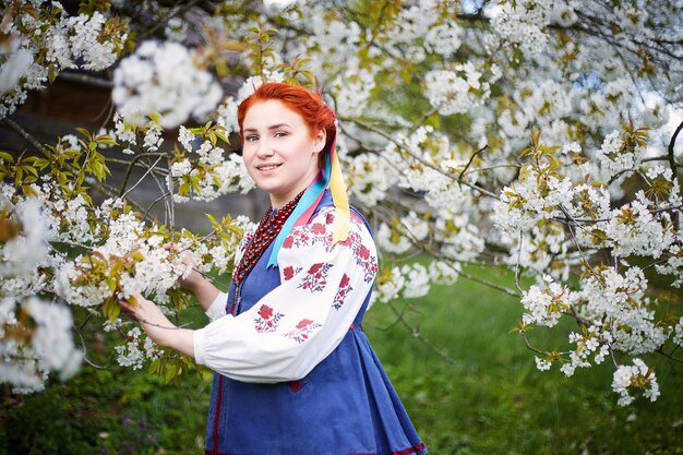 Mujer joven en traje nacional ucraniano Sonriente joven dama en ropa tradicional Manténgase cerca del árbol floreciente Paz en Ucrania