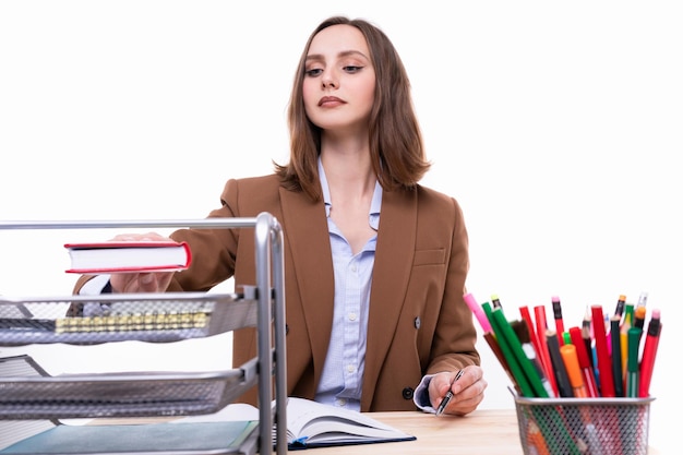 Una mujer joven con un traje de negocios marrón busca documentos en un estante en el escritorio Estudio de negocios disparando sobre un fondo blanco