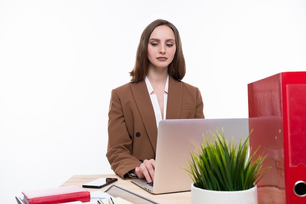 Una mujer joven en un traje de negocios trabajando en una computadora portátil sobre un fondo blanco. Aislado