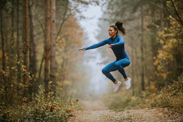 Mujer joven en traje de pista azul tomando salto de altura en la pista forestal en otoño