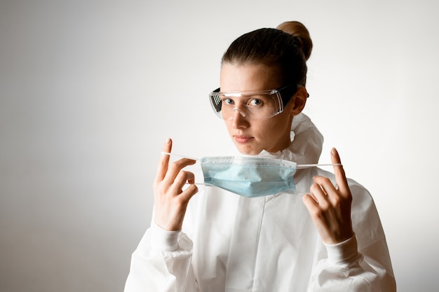 Foto mujer joven en traje de protección y gafas tiene máscara médica azul