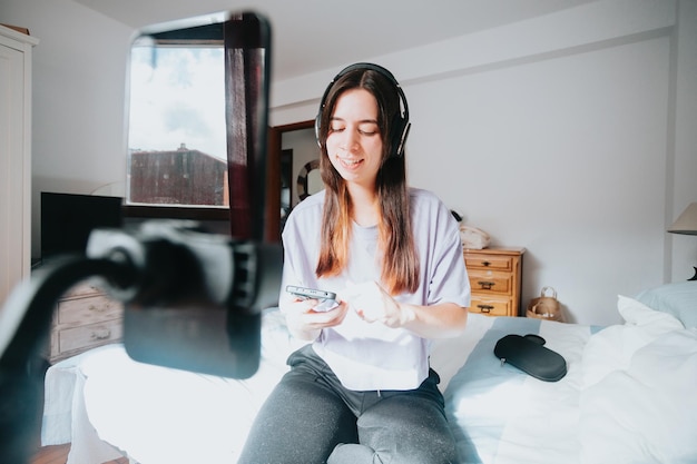 Mujer joven transmitiendo en su dormitorio explicando cosas mientras escucha música Joven streamer trabajando