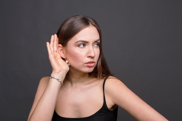 Mujer joven tratando de escuchar chismes. Chica muy curiosa sosteniendo su mano cerca de la oreja, tratando de escuchar algo