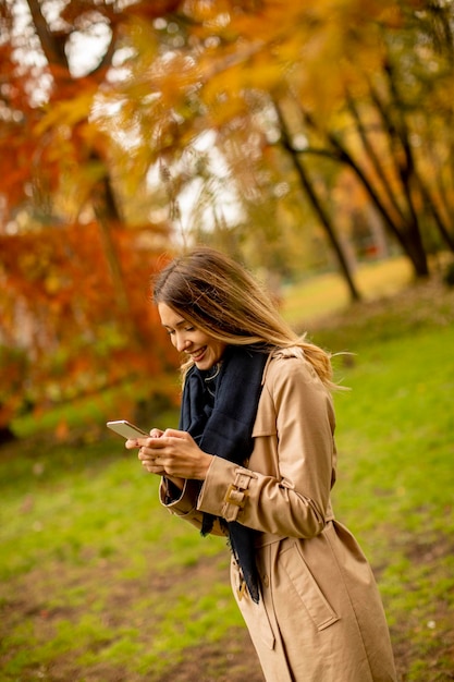 Mujer joven a través de teléfono móvil en el parque de otoño