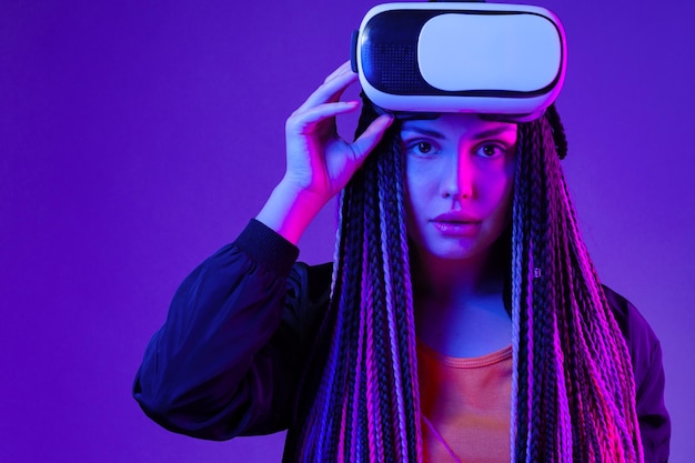 Mujer joven con trenzas afro con gafas vr sobre fondo de neón púrpura oscuro