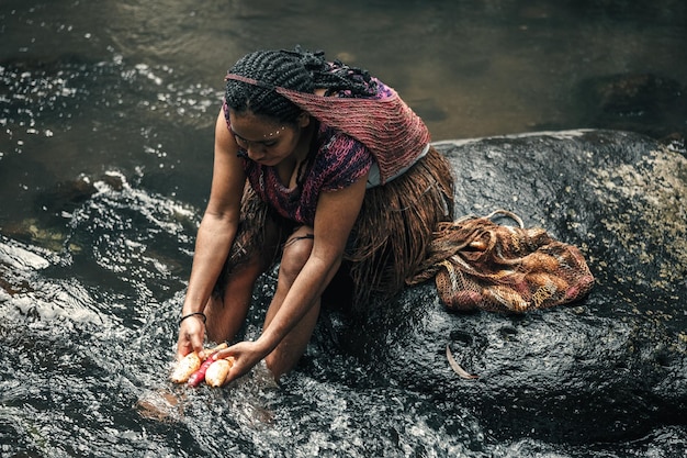 Mujer joven de una tribu papú está lavando batatas en el río