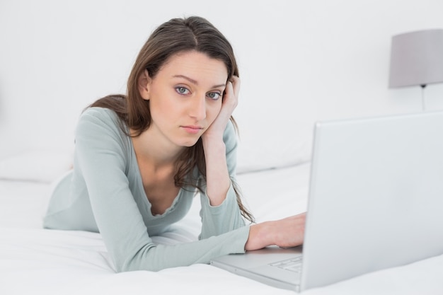 Foto mujer joven triste casual usando la computadora portátil en la cama