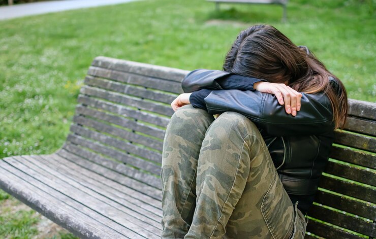 Mujer joven triste y deprimida situada en un banco del parque con los brazos y la cabeza sobre las rodillas