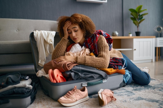 Mujer joven triste y equipaje de vacaciones desempaquetado